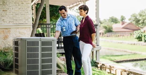 HVAC technician reviewing an outdoor condenser with a homeowner
