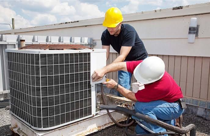Two technicians servicing a rooftop air conditioning condenser