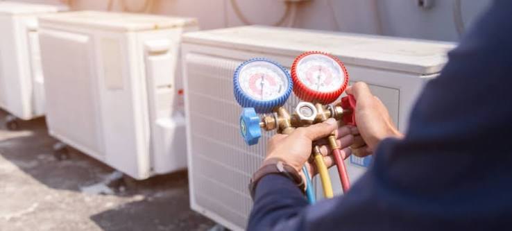 Technician holding refrigerant manifold gauges at a bank of outdoor AC units