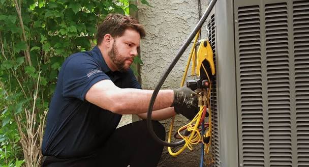 Technician connecting diagnostic gauges to a rooftop HVAC unit